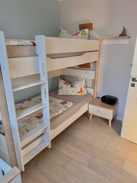 Ein Etagenbett im zweiten Schlafzimmer. Das Bettgestell aus Holz ist weiß. Daneben steht ein Nachttischchen.