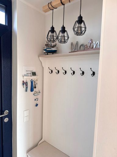 Eine Garderobe neben der Eingangtür mit Sitzbank, Sechs Haken und darüber eine Lampe.