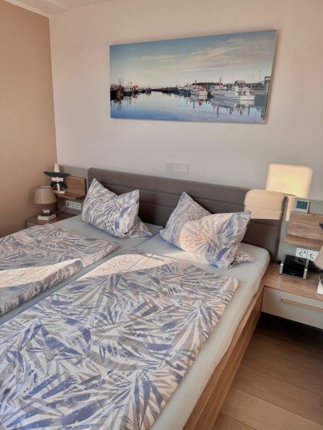 Ein Doppelbett im Schlafzimmer mit Lämpchen auf den Nachttischen auf beiden Seiten. Das Bett ist schön bezogen.