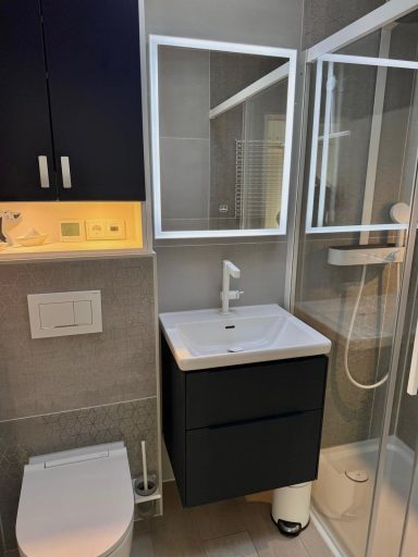 Ein Badezimmer mit Waschtisch mit 2 Schubladen, Ein großer Spiegel inklusive Beleuchtung, eine Glaswand hinter der eine Regendusche ist.