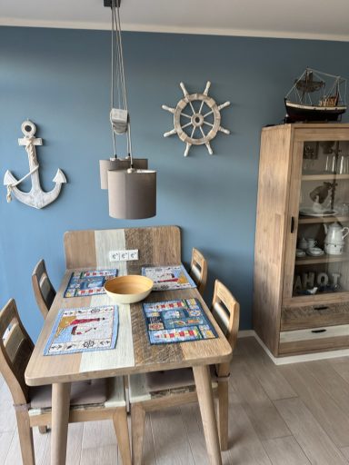 Esstisch mit Vier Stühlen. Auf dem Tisch liegen Vier Unterleger und eine Obstschüssel in der Mitte des Tisches über dem eine Lampe hängt