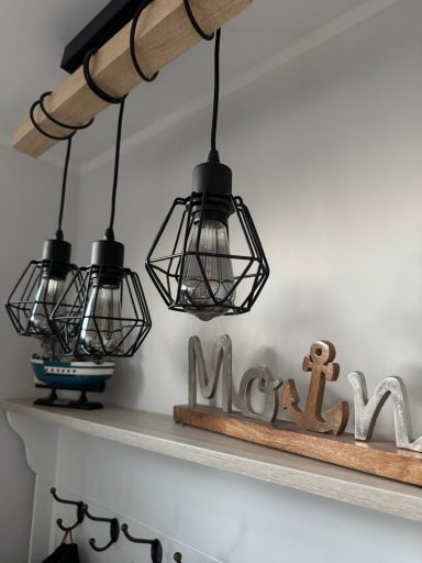 Eine Lampe mit frei hängenden Leuchten umfasst von schwarzem Gitter. dahinter ein dekorativer Spruch "Moin" und ein kleiner Deko-Fischkutter