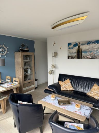 Wohn- / Essbereich. Wieder das Doppelsofa und Sessel. Im Hintergrund ein Esstisch, Vier Stühlen, Vitrine mit Gläsern, Maritime Deko.