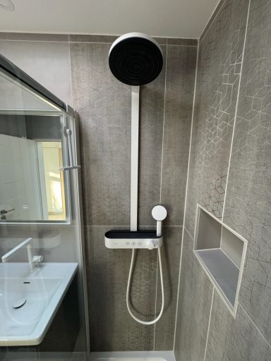 Eine weiße Regendusche mit zusätzlicher Handbrause. Links eine kleine Nische in der Wand zum abstellen von Shampoo.